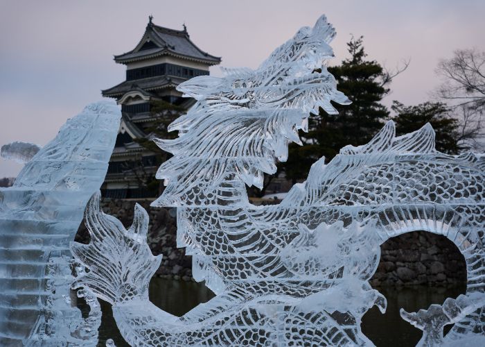 An ice sculpture of an East Asian dragon backed by a view of Matsumoto Castle in wintertime